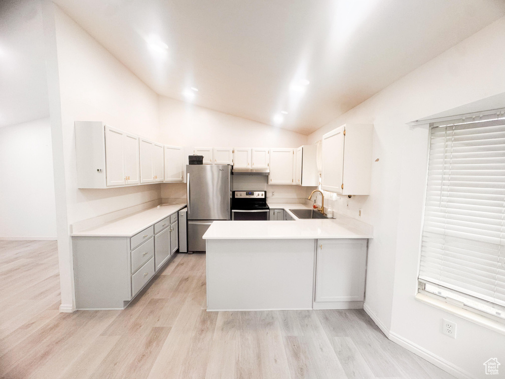 Kitchen featuring stainless steel appliances, lofted ceiling, light wood-type flooring, a peninsula, and light countertops