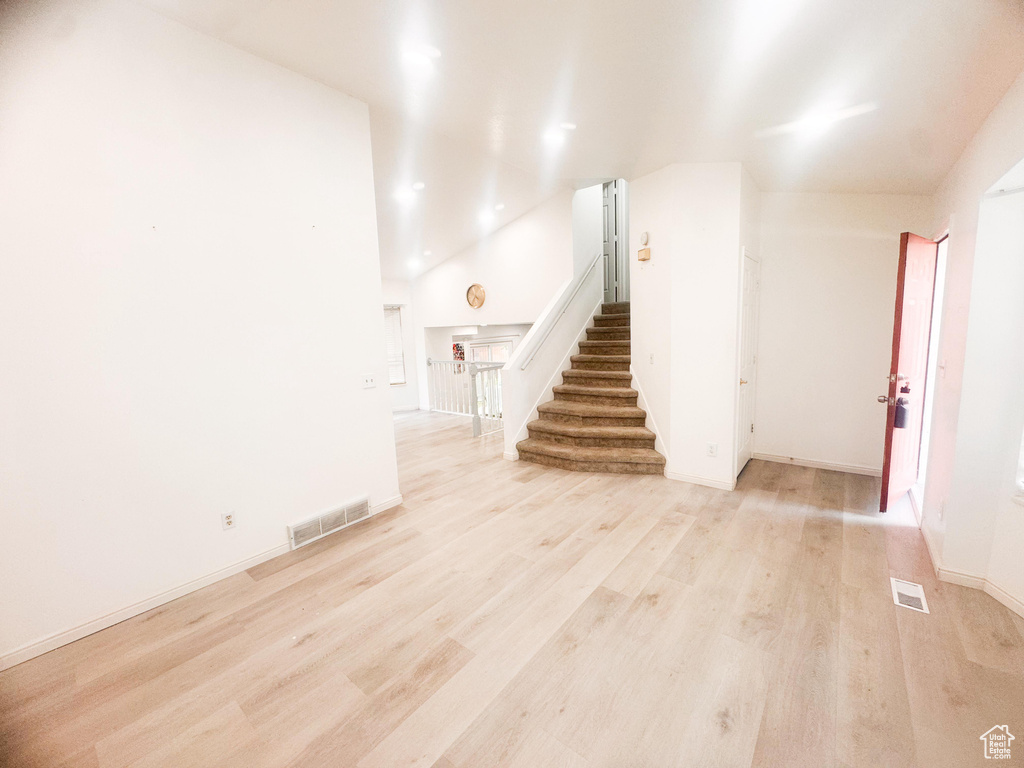 Unfurnished living room featuring stairs, light wood-type flooring, lofted ceiling, and recessed lighting