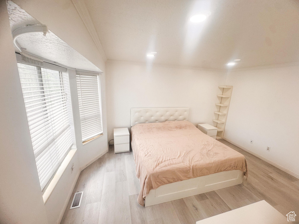 Bedroom with multiple windows, light wood-style floors, ornamental molding, and recessed lighting