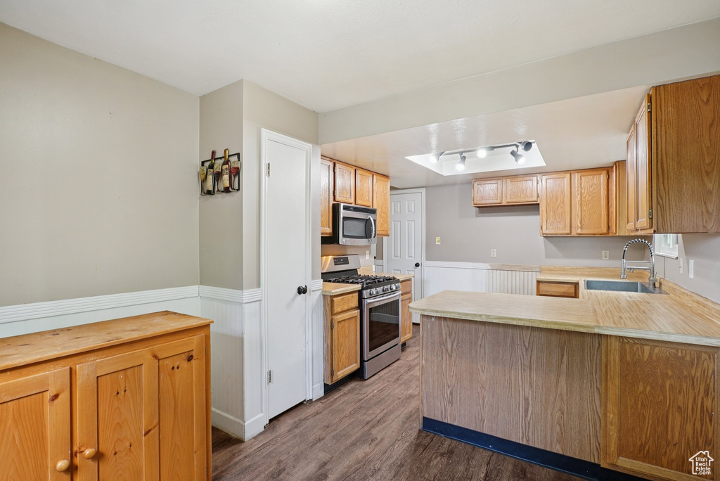 Kitchen with appliances with stainless steel finishes, dark wood-style flooring, a peninsula, wainscoting, and light countertops