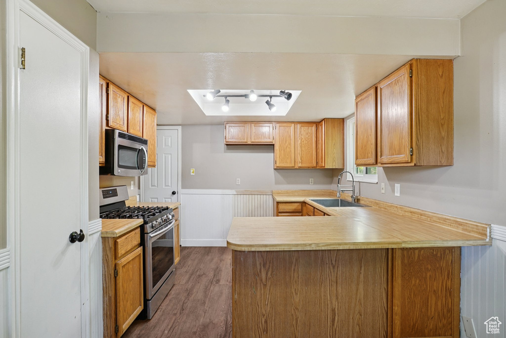 Kitchen with stainless steel appliances, a peninsula, light countertops, dark wood finished floors, and wainscoting