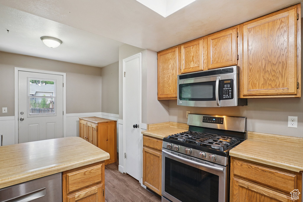 Kitchen with stainless steel appliances, wood finished floors, light countertops, and a skylight