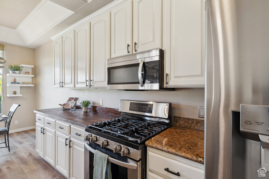 Kitchen with appliances with stainless steel finishes, light wood-style flooring, dark stone countertops, and white cabinets