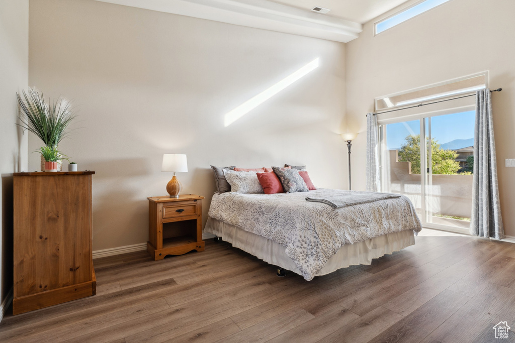 Bedroom featuring access to outside, wood finished floors, multiple windows, and a high ceiling