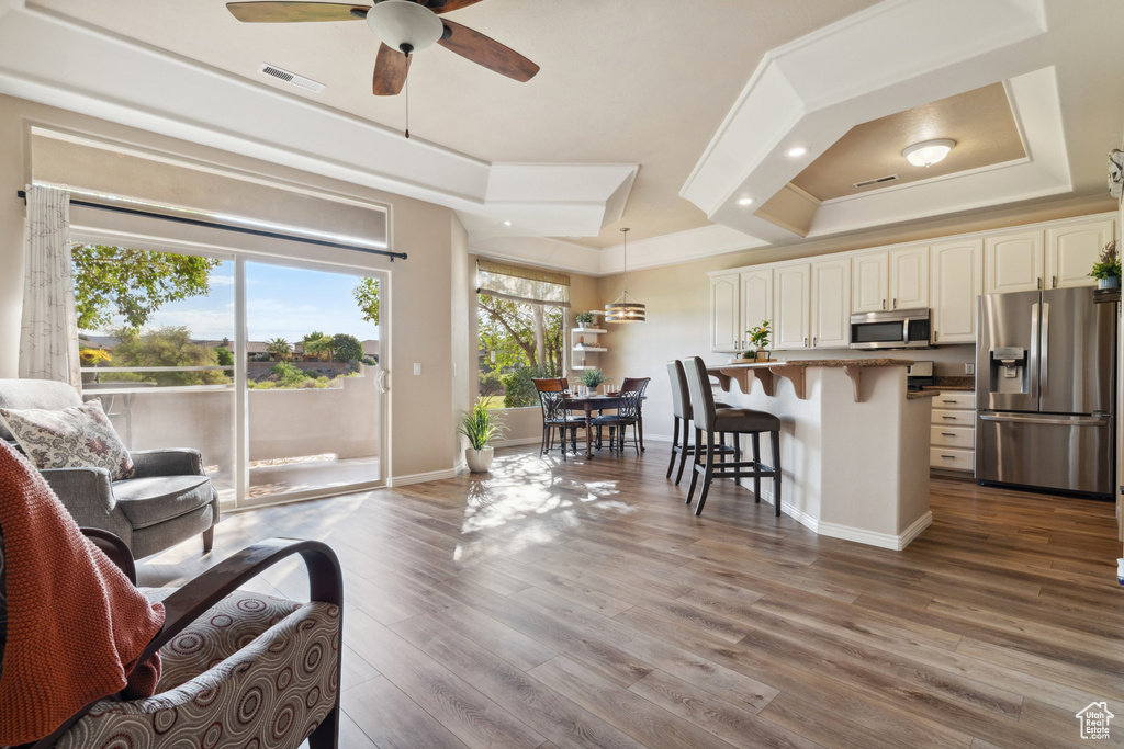 Living room featuring a ceiling fan, a raised ceiling, ornamental molding, and dark wood-style floors