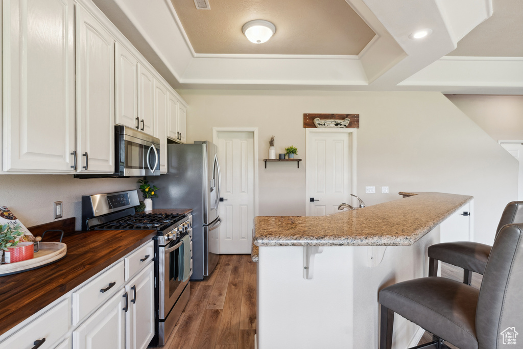 Kitchen featuring stainless steel appliances, wood counters, a kitchen bar, and white cabinets