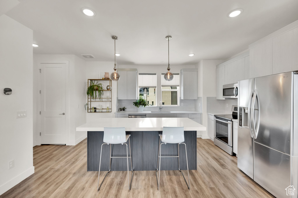 Kitchen featuring appliances with stainless steel finishes, a sink, a breakfast bar, a kitchen island, and light wood-style floors