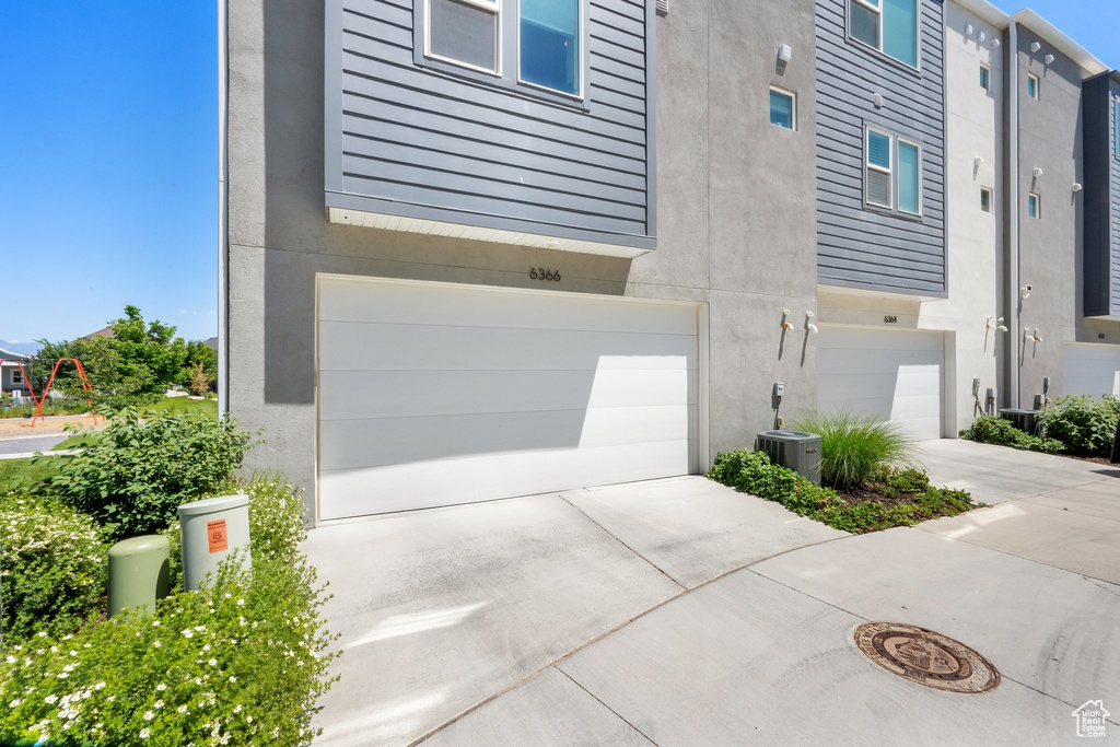 View of side of home with stucco siding, an attached garage, driveway, and central air condition unit
