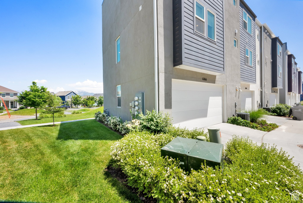 View of side of property with a residential view, a garage, central AC unit, a yard, and stucco siding