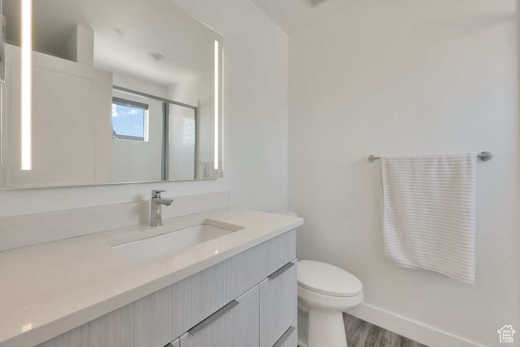 Bathroom featuring vanity, toilet, wood finished floors, baseboards, and an enclosed shower