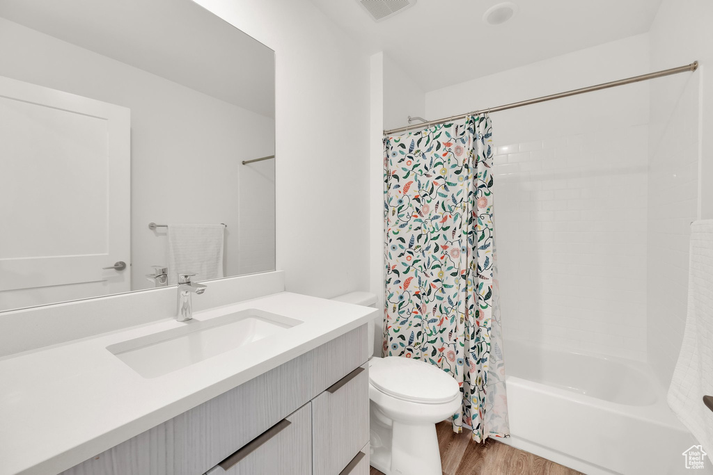 Bathroom with vanity, wood finished floors, toilet, and shower / tub combo