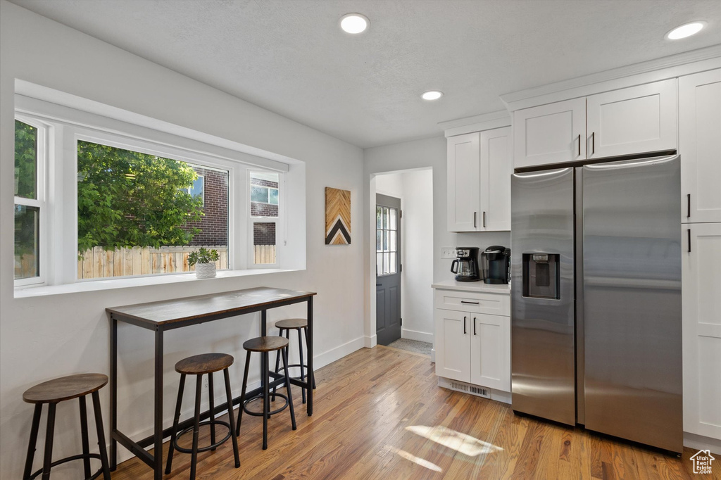 Kitchen featuring stainless steel fridge with ice dispenser, recessed lighting, white cabinets, a breakfast bar area, and light wood-style floors