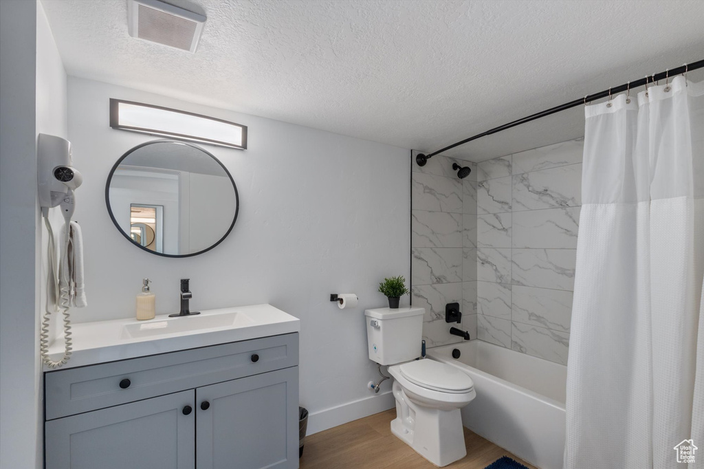 Bathroom featuring a textured ceiling, vanity, wood finished floors, and shower / bath combo with shower curtain