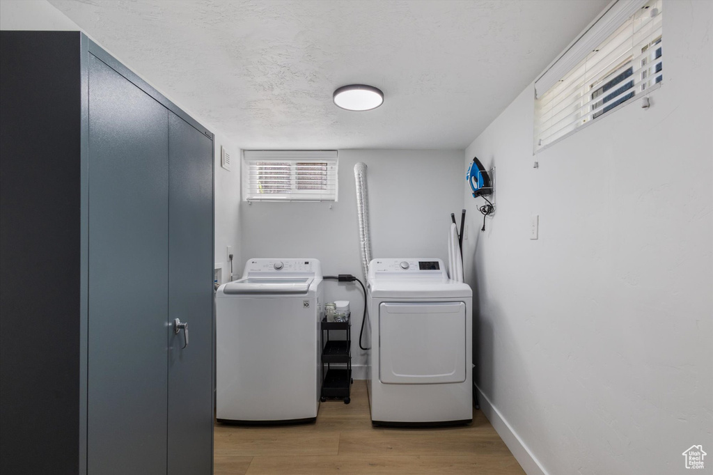 Laundry room with washing machine and dryer, light wood finished floors, and a textured ceiling