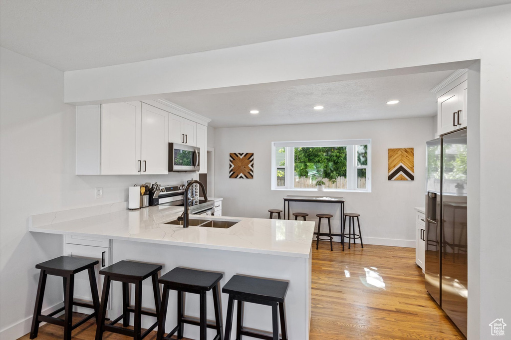 Kitchen featuring appliances with stainless steel finishes, light countertops, a breakfast bar, white cabinets, and a peninsula
