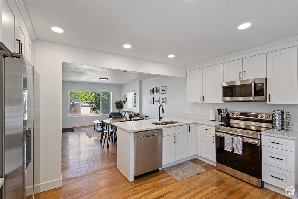 Kitchen with stainless steel appliances, a peninsula, white cabinets, light countertops, and light wood-style floors