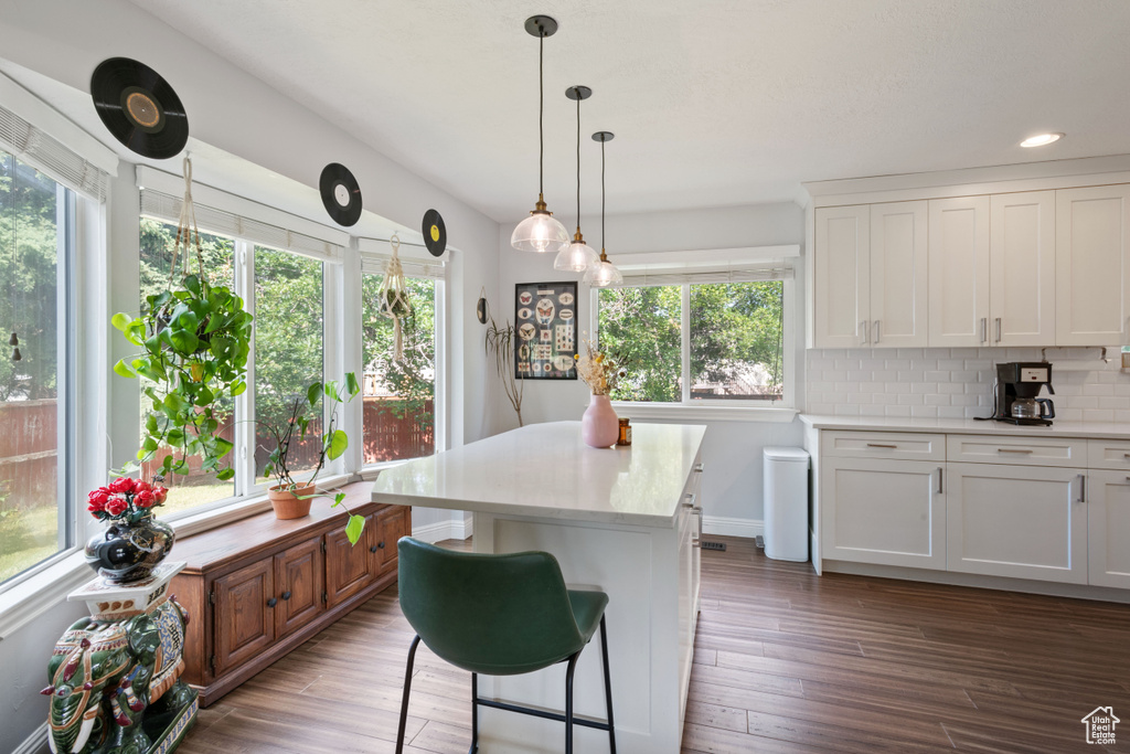 Kitchen featuring light countertops, white cabinets, wood finished floors, decorative backsplash, and hanging light fixtures
