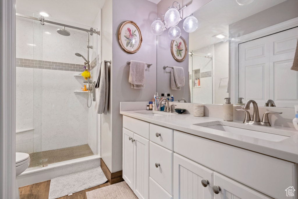 Full bath with a shower stall, double vanity, wood finished floors, and toilet