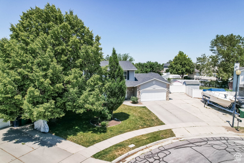 View of property hidden behind natural elements featuring driveway, an attached garage, stone siding, and a front yard