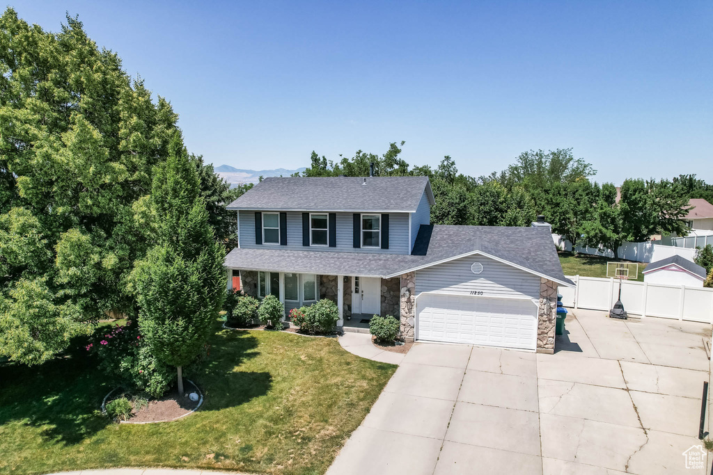 Traditional home featuring stone siding, a garage, driveway, roof with shingles, and a porch