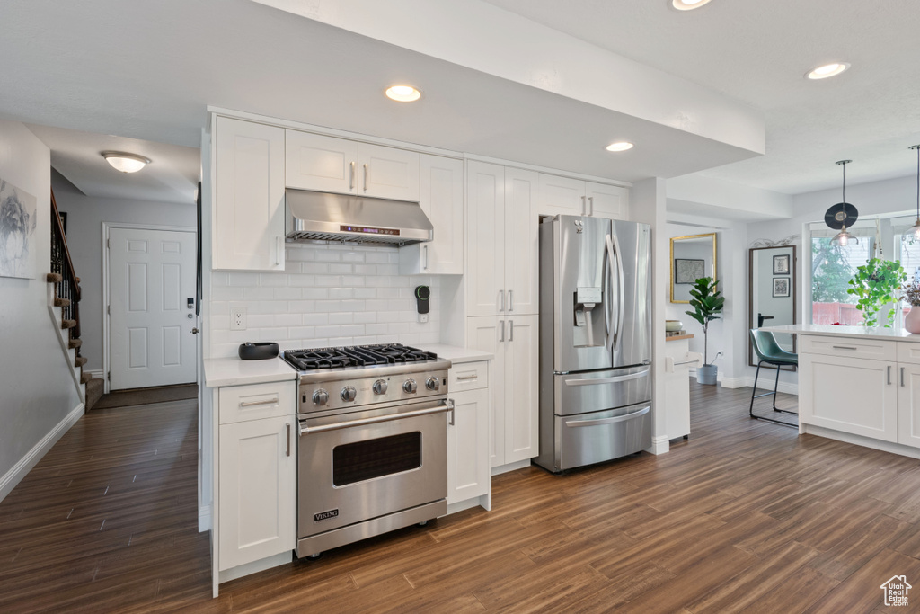 Kitchen with stainless steel appliances, under cabinet range hood, baseboards, white cabinetry, and recessed lighting