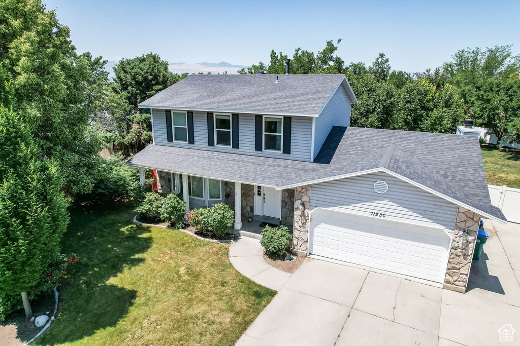 View of front facade featuring stone siding, roof with shingles, a garage, driveway, and covered porch