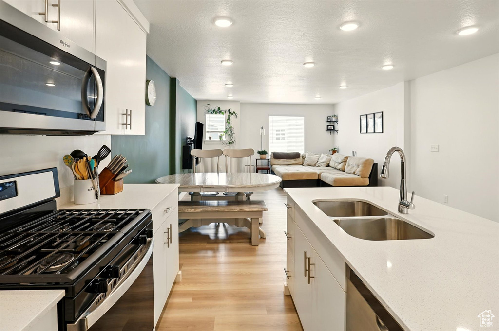 Kitchen with stainless steel appliances, light wood-style flooring, white cabinetry, light stone countertops, and recessed lighting