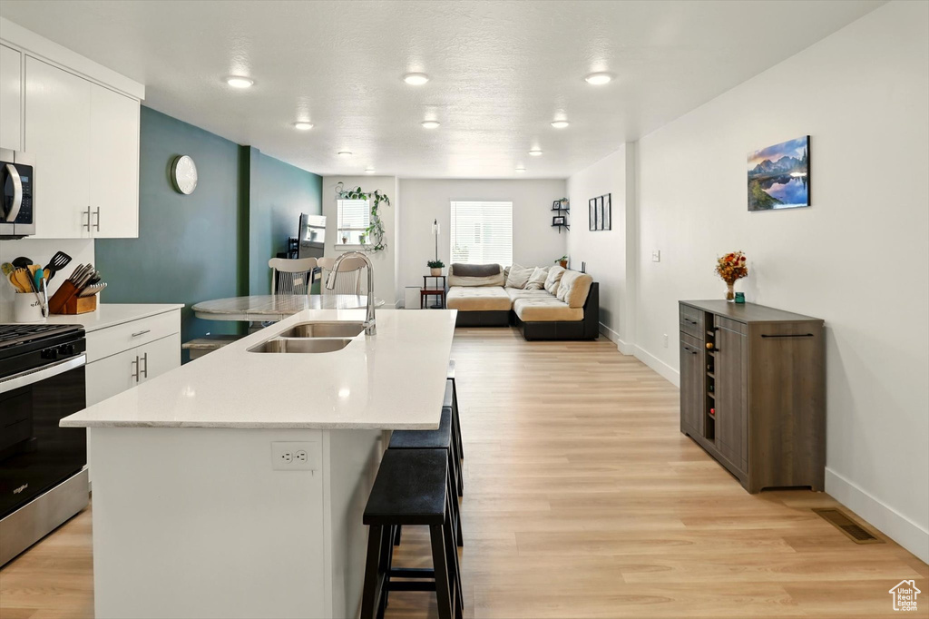 Kitchen with stainless steel appliances, a breakfast bar, a kitchen island with sink, light wood-style flooring, and white cabinetry