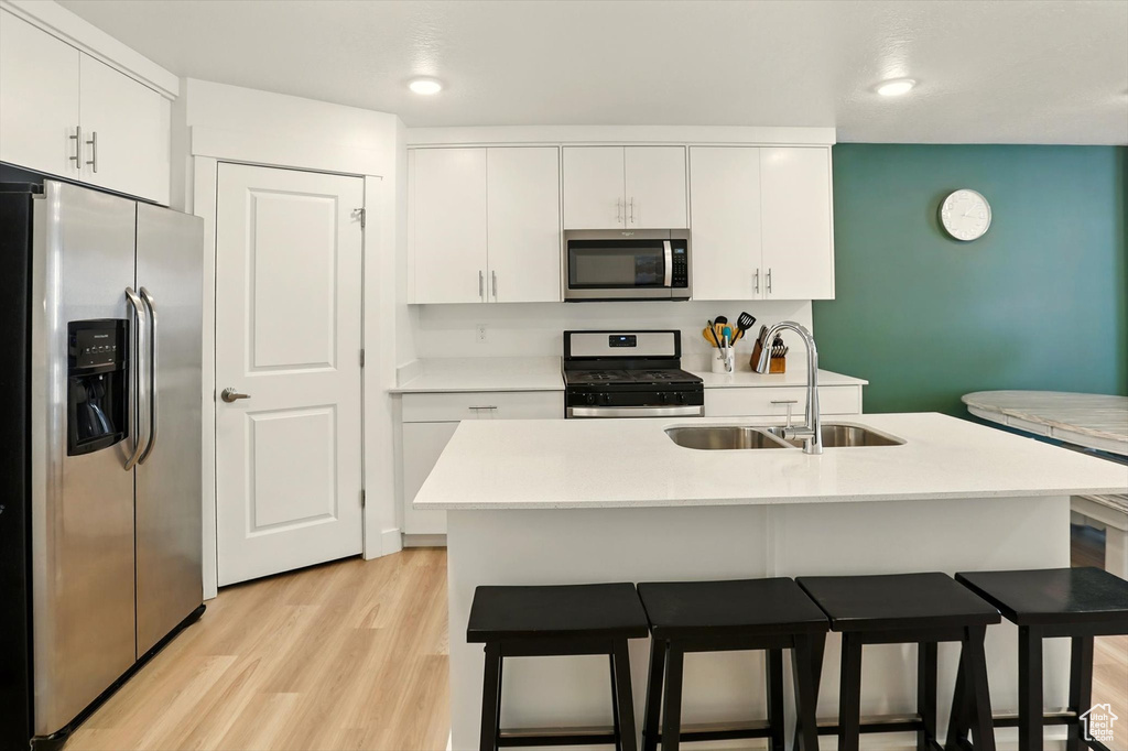 Kitchen featuring stainless steel appliances, a kitchen bar, white cabinetry, light wood-style floors, and recessed lighting