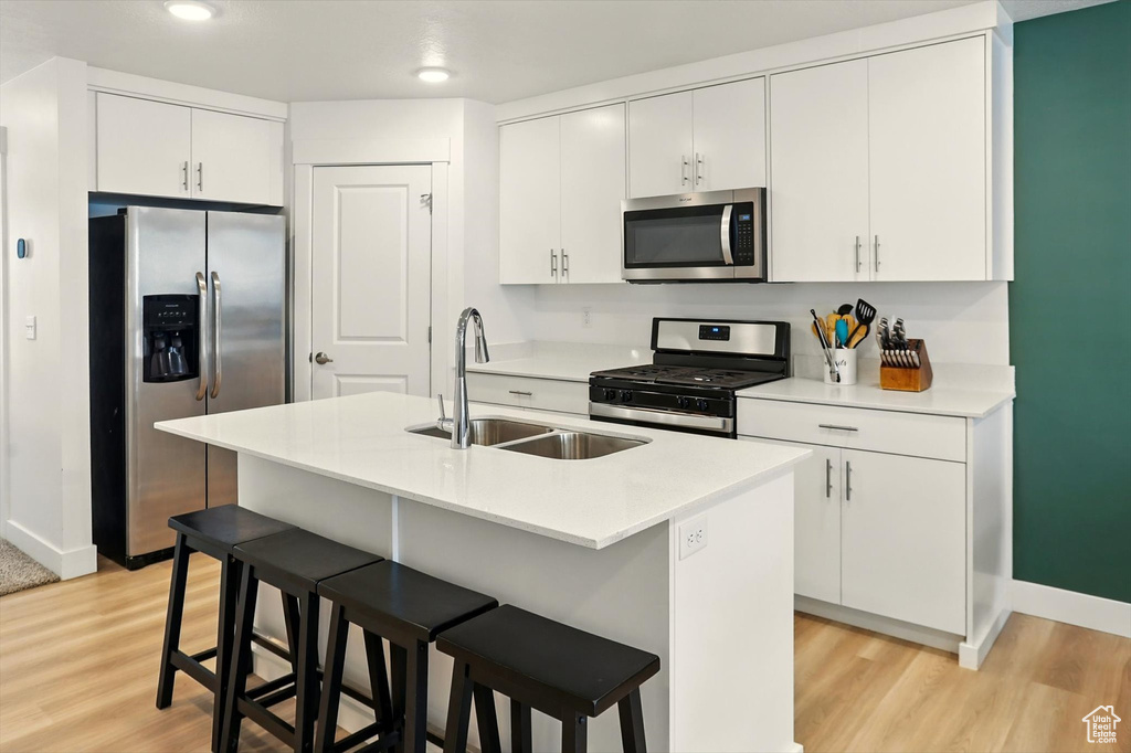 Kitchen with stainless steel appliances, light wood-style floors, a breakfast bar, light countertops, and recessed lighting