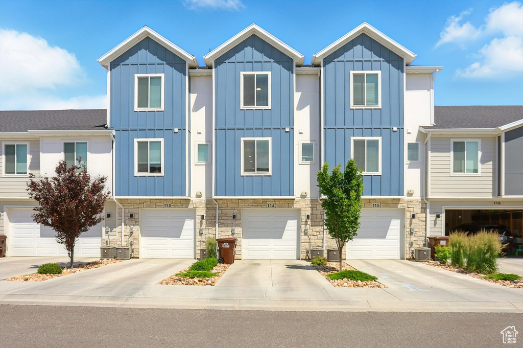 Townhome / multi-family property with stone siding, driveway, an attached garage, and board and batten siding