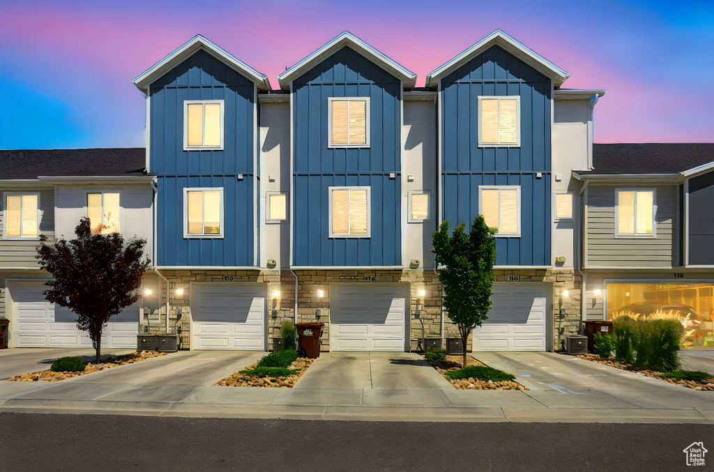 Townhome / multi-family property with board and batten siding, driveway, a garage, and stone siding