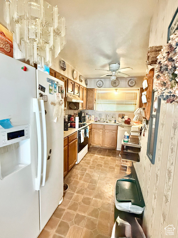 Kitchen with white appliances, under cabinet range hood, light countertops, ceiling fan, and brown cabinetry