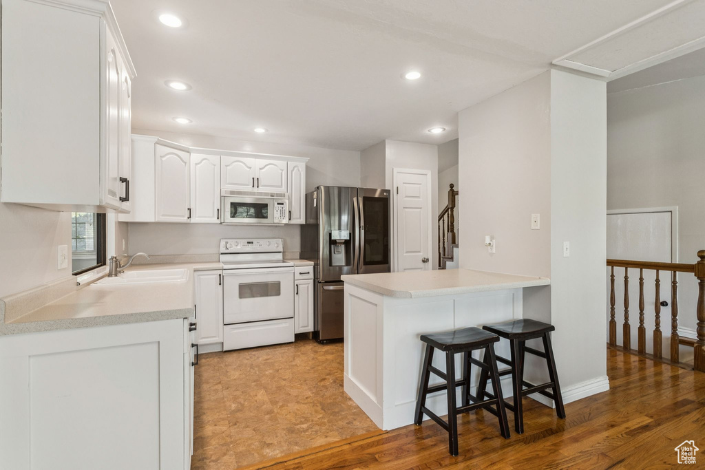 Kitchen featuring white appliances, a peninsula, recessed lighting, white cabinets, and a kitchen breakfast bar