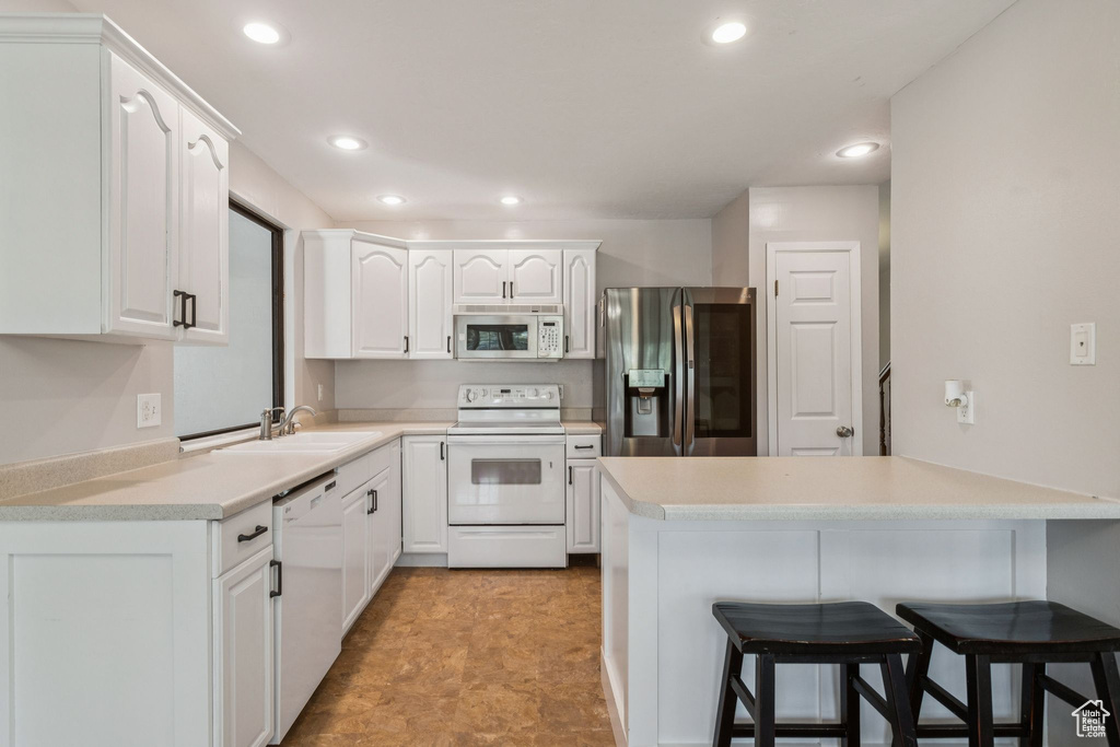 Kitchen with white appliances, a peninsula, a kitchen bar, white cabinetry, and recessed lighting