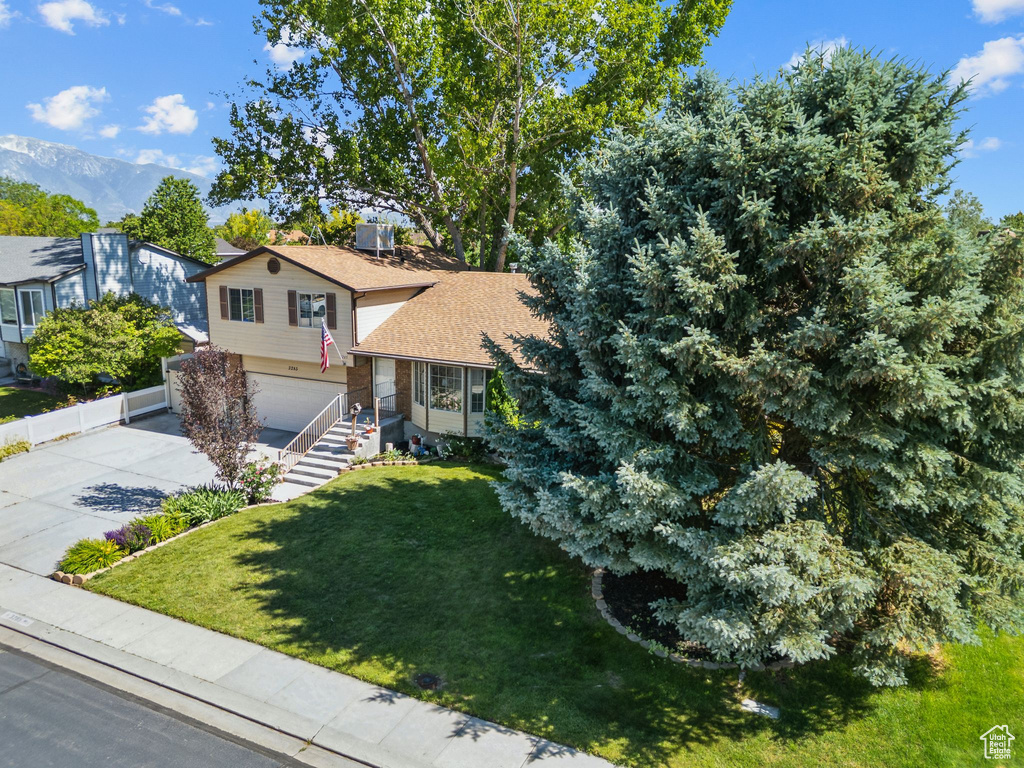 Tri-level home featuring a front lawn, an attached garage, driveway, and roof with shingles