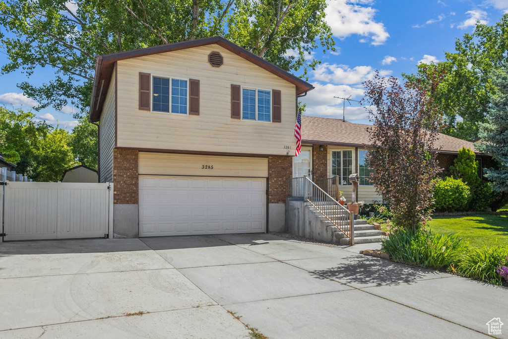 Tri-level home with brick siding, an attached garage, concrete driveway, and a shingled roof