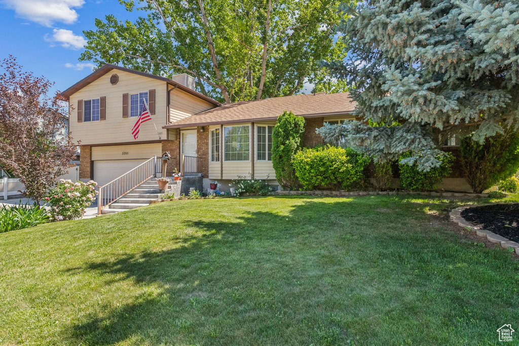 Split level home featuring an attached garage, a front lawn, and brick siding