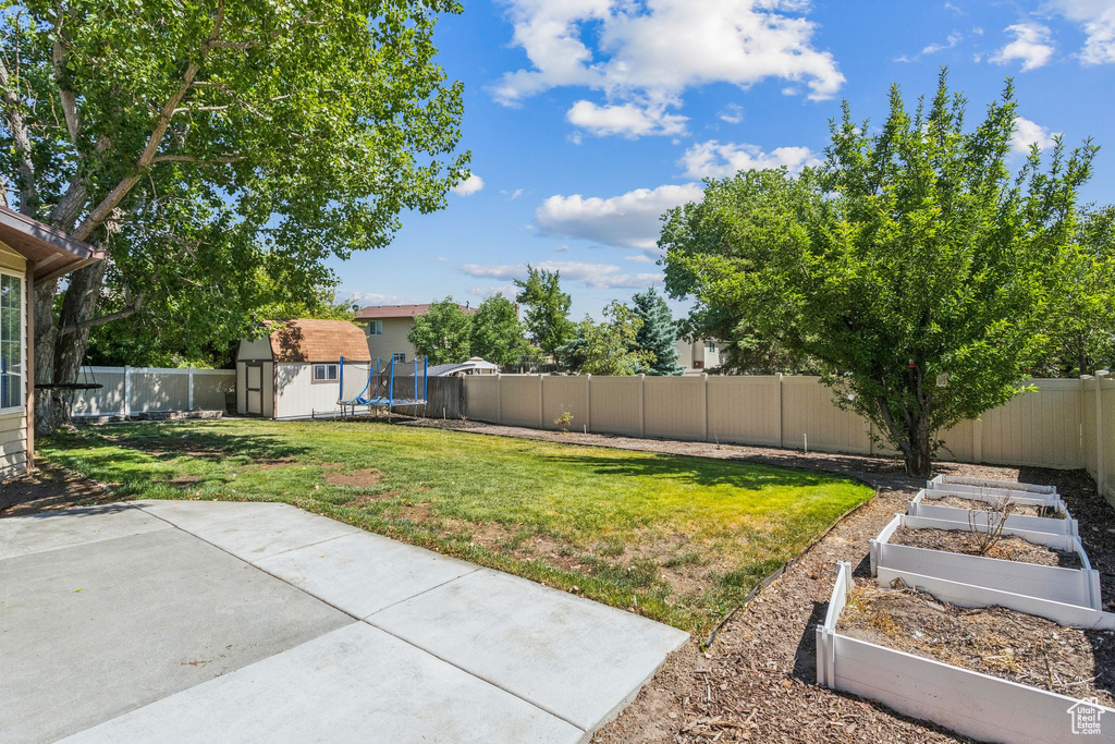 Fenced backyard with a garden, a storage shed, and a patio area