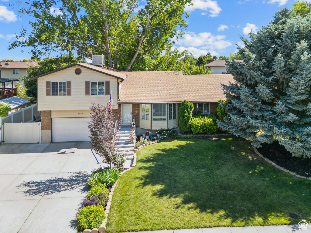 Tri-level home with a garage, driveway, brick siding, and a chimney