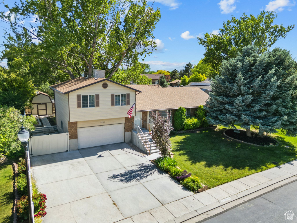 Tri-level home with an attached garage, driveway, brick siding, and a front lawn