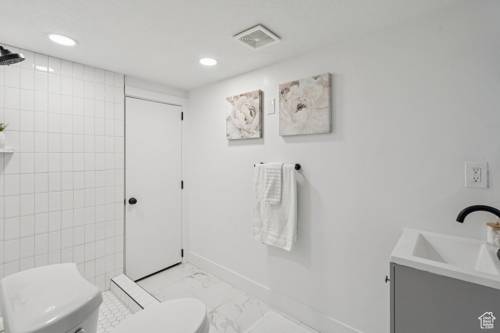 Bathroom featuring toilet, marble look tile flooring, vanity, baseboards, and recessed lighting
