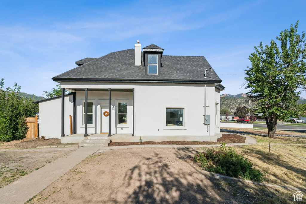 Rear view of property featuring stucco siding, roof with shingles, and a chimney