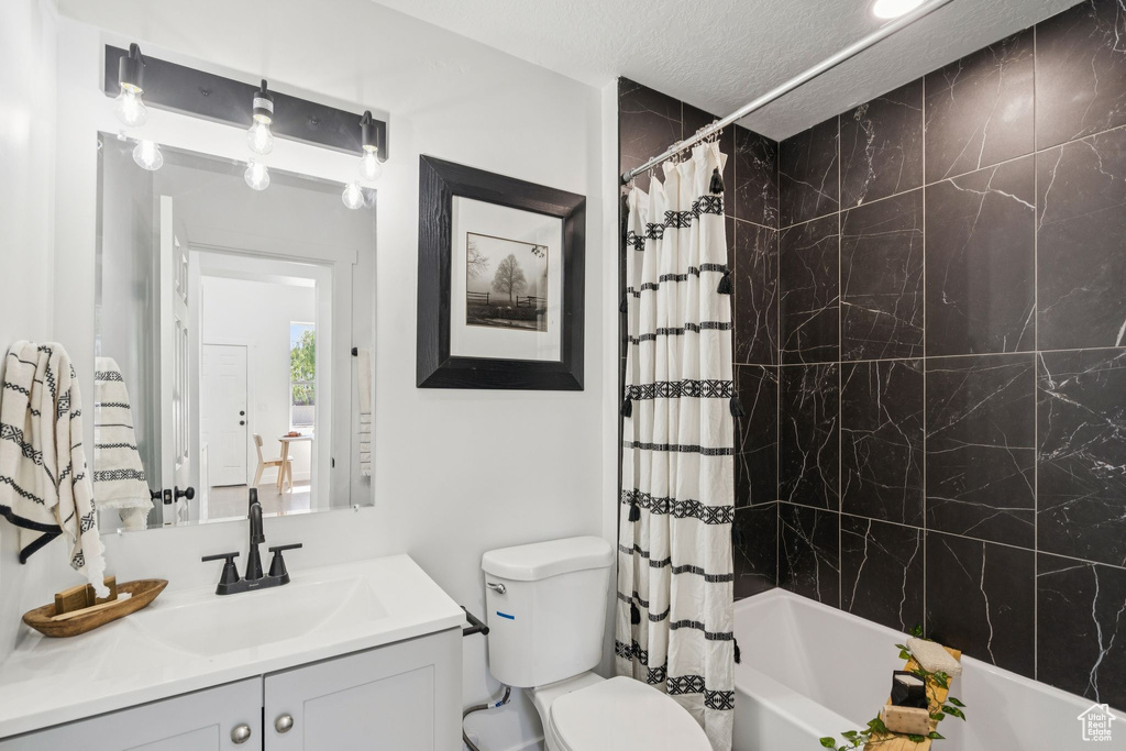 Bathroom featuring toilet, vanity, shower / tub combo with curtain, and a textured ceiling