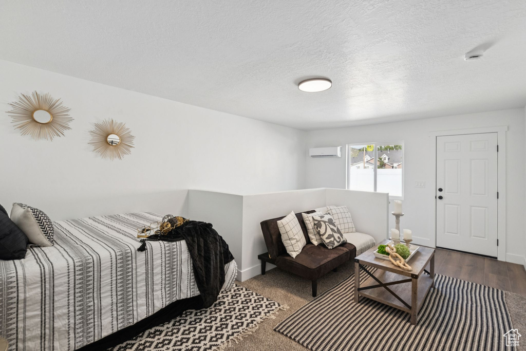 Living area with an AC wall unit, wood finished floors, baseboards, and a textured ceiling