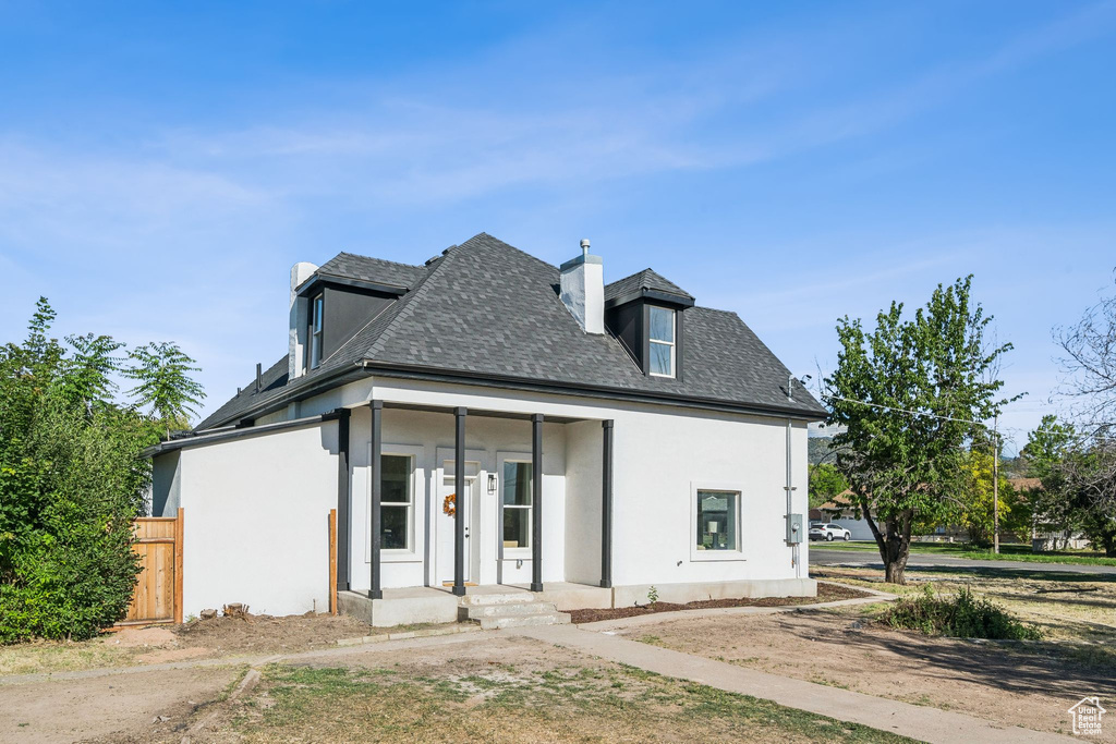 View of front facade featuring a chimney, stucco siding, and a shingled roof