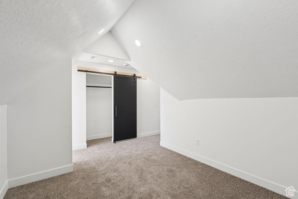 Additional living space featuring a barn door, lofted ceiling, baseboards, carpet floors, and a textured ceiling