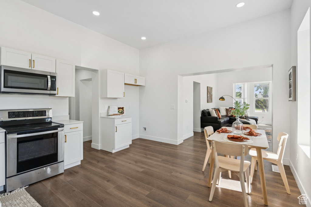 Kitchen featuring stainless steel appliances, light countertops, dark wood-type flooring, white cabinetry, and open floor plan