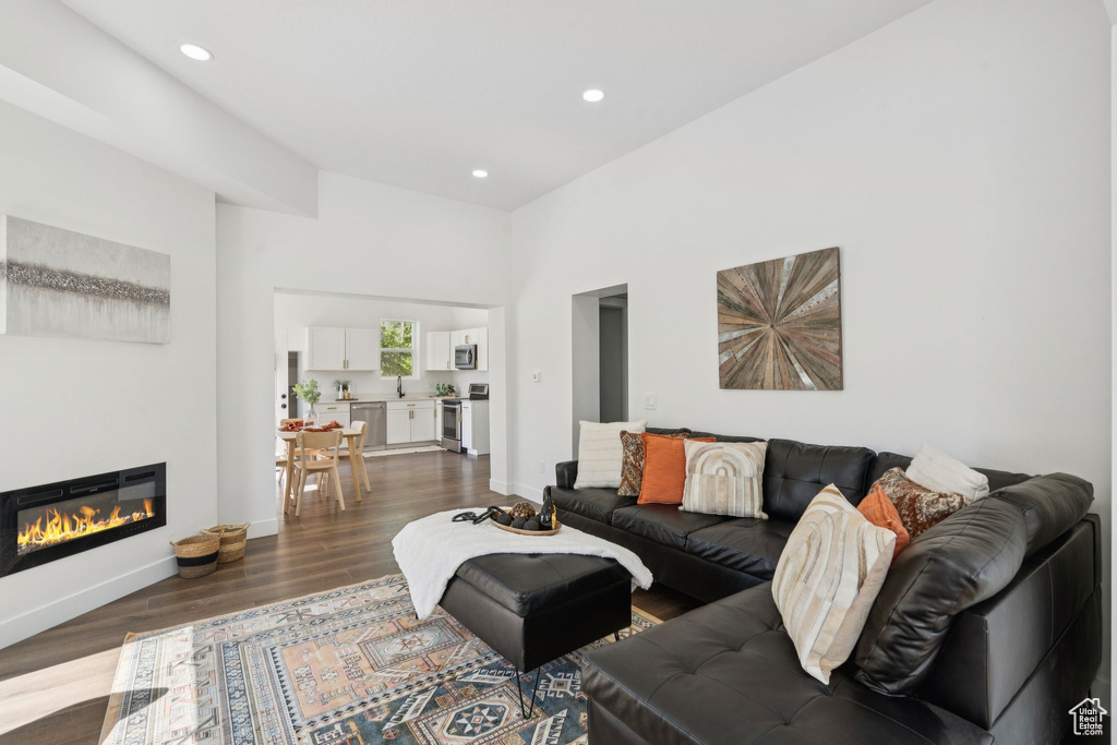 Living room featuring dark wood-style flooring, recessed lighting, baseboards, a glass covered fireplace, and a high ceiling