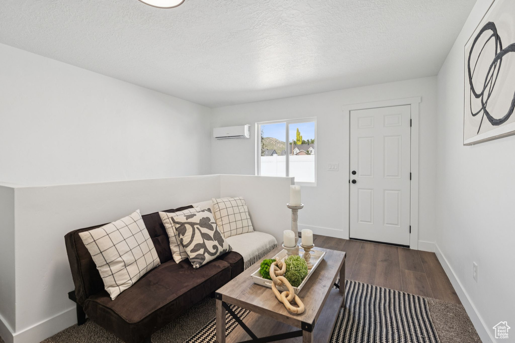 Living room featuring an AC wall unit, baseboards, wood finished floors, and a textured ceiling
